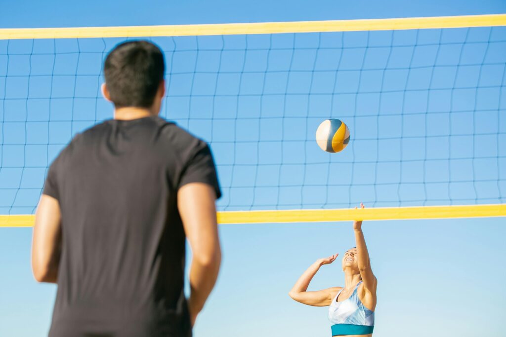 A man and woman playing volleyball on the beach under a clear blue sky.
